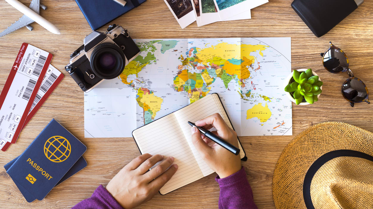 A woman is sitting at a table with a map, hat, and other travel items.