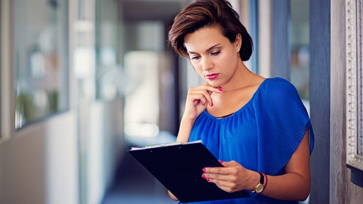 A business woman looking at a clipboard in an office.