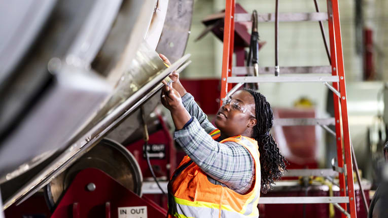 A woman working on a metal pipe in a factory.