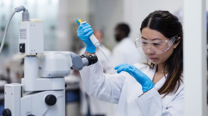 A woman in a lab coat working with a microscope.