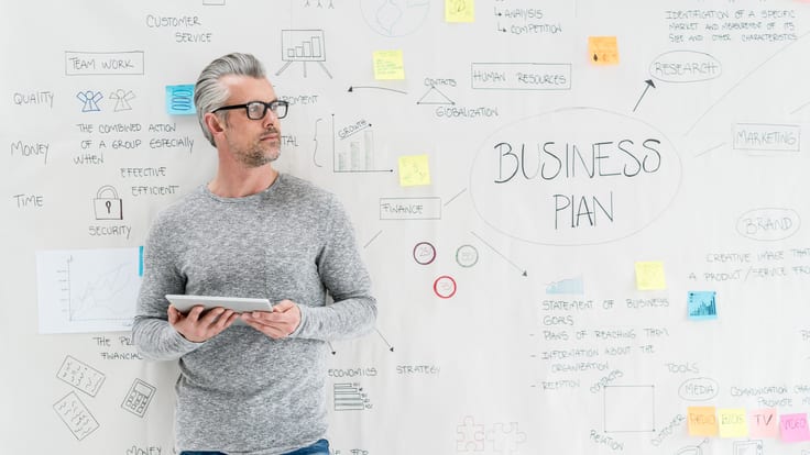 A man standing in front of a whiteboard with a business plan written on it.