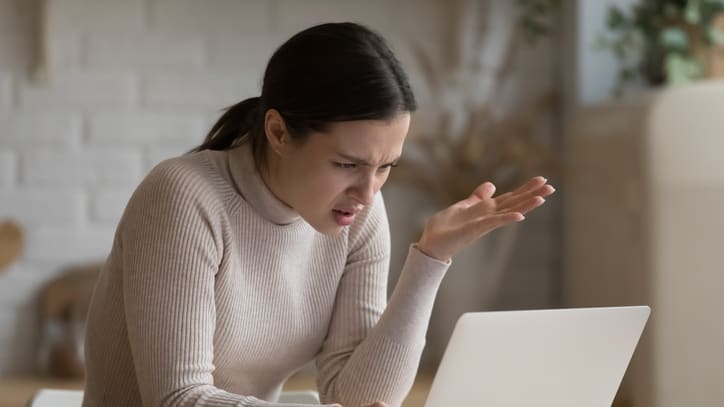 A woman is yelling at her laptop while sitting at a table.