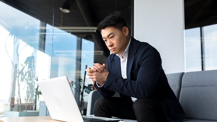 A young businessman sitting on a couch with a laptop.