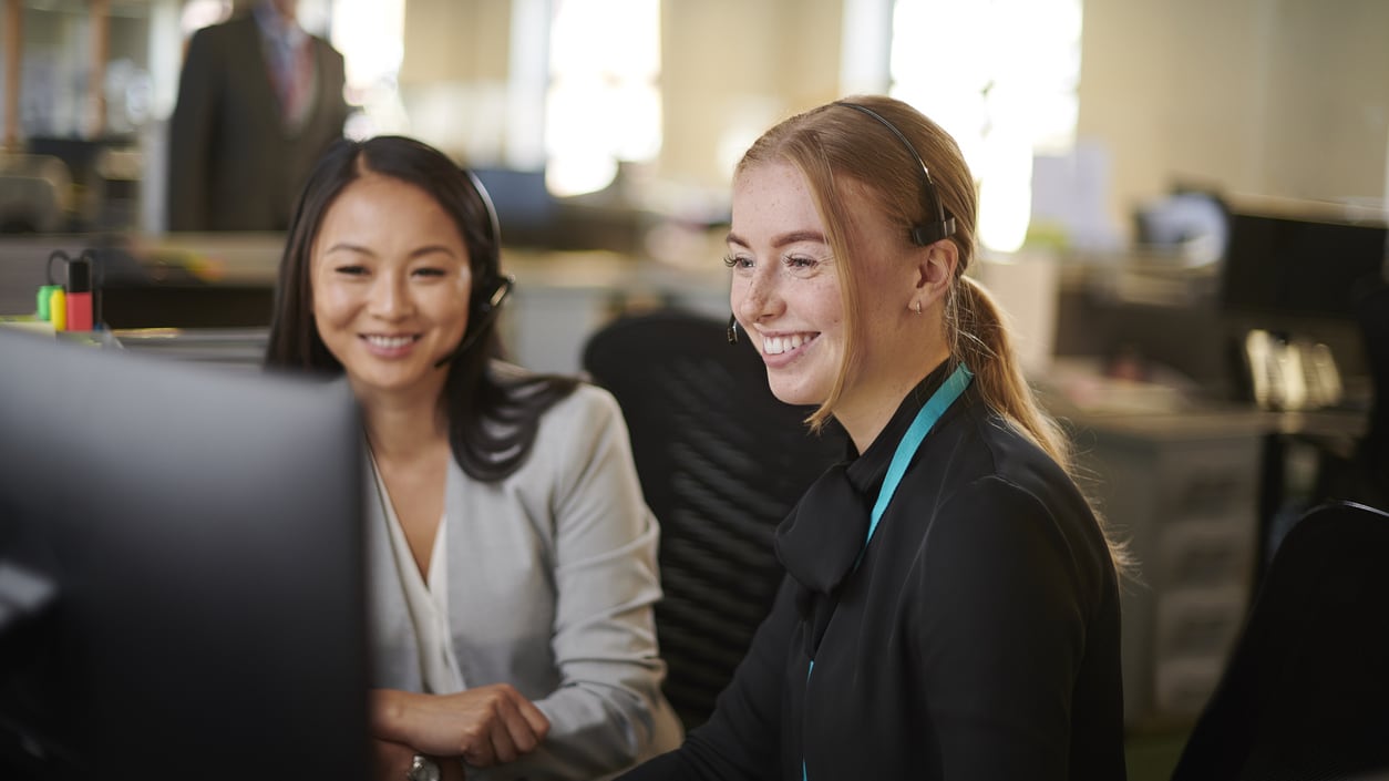 Two women working at a computer in an office.