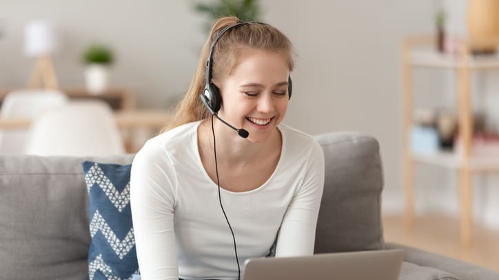 A woman wearing a headset is sitting on a couch and using a laptop.