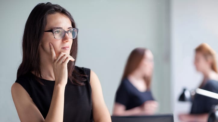 A woman in glasses is standing in front of a group of people in an office.