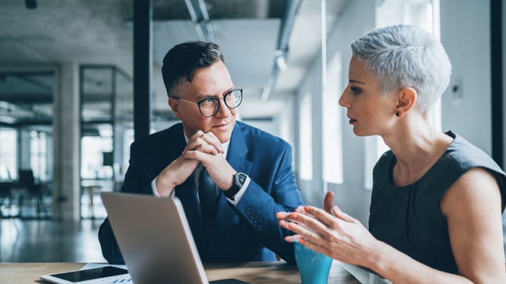 Two business people talking at a table with a laptop.