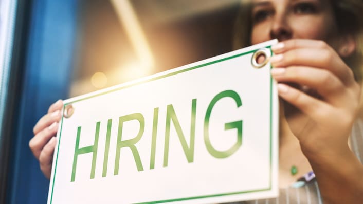 A woman holding up a hiring sign.