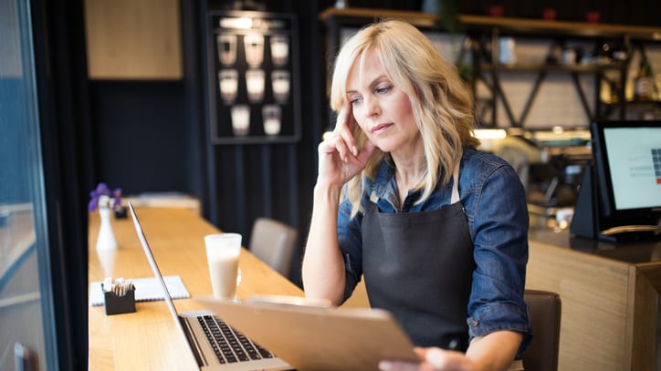 A woman in a apron sitting at a table with a laptop.