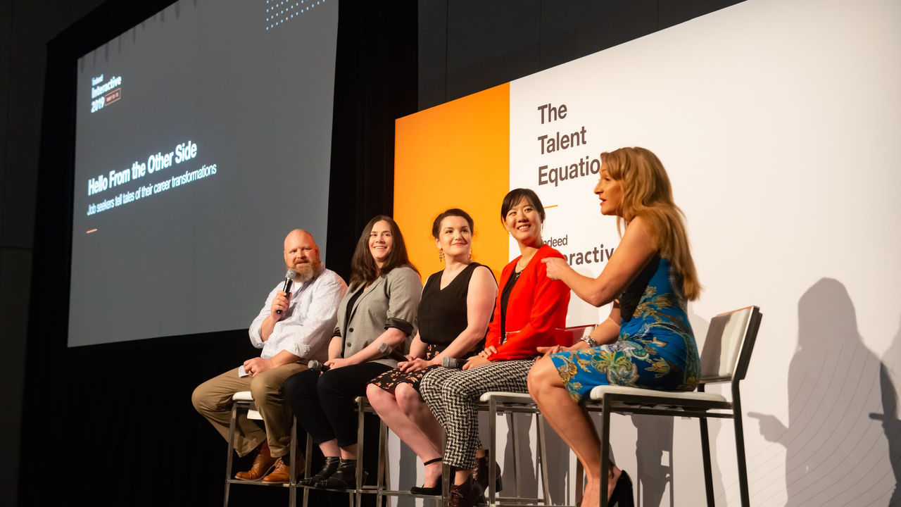 A group of people sitting on stools at a conference.