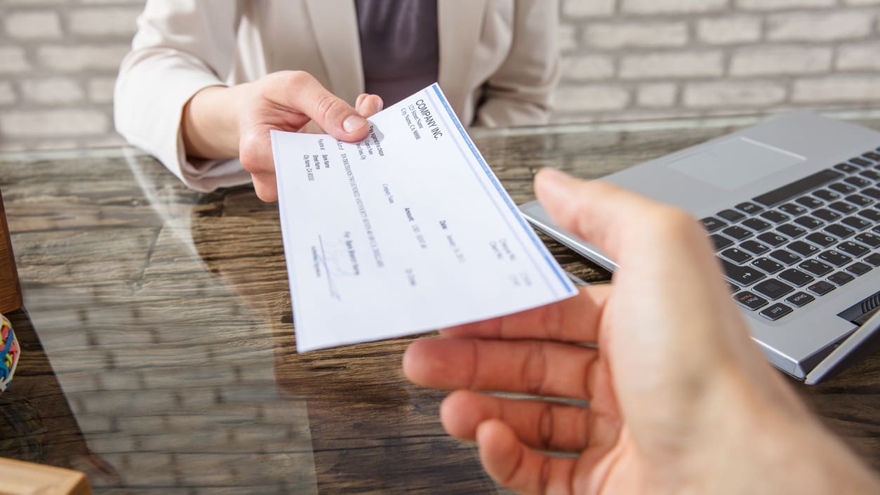 A person handing a check to another person at a desk.