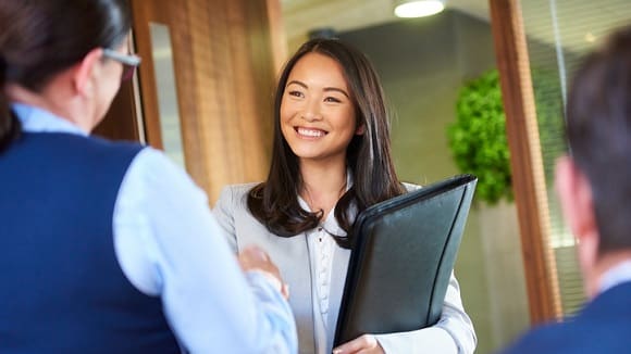 A business woman shakes hands with another woman in an office.