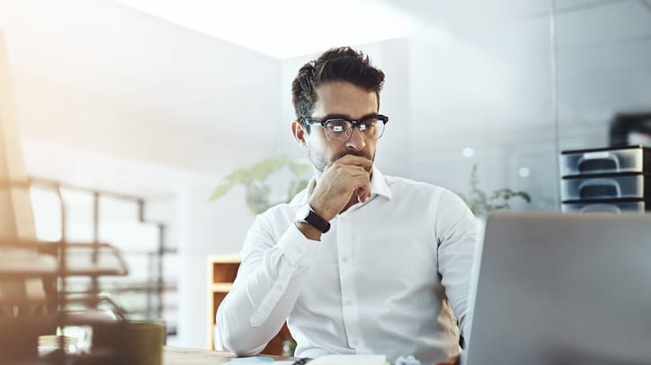 A man in glasses is sitting in front of a laptop.