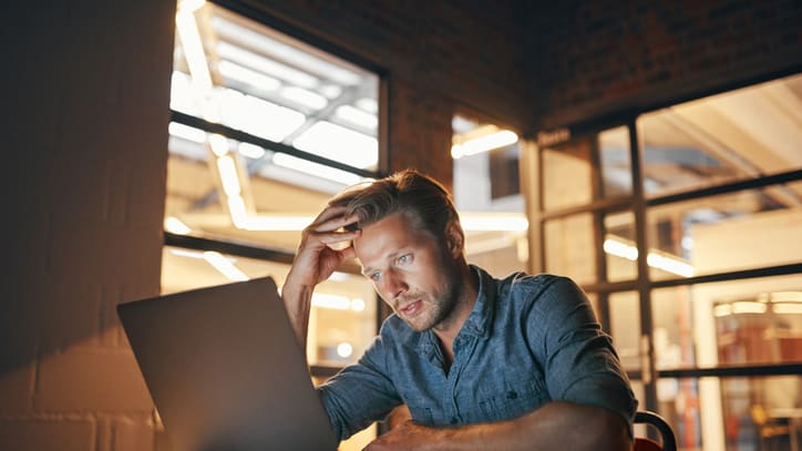 A man sitting at a desk looking at his laptop.