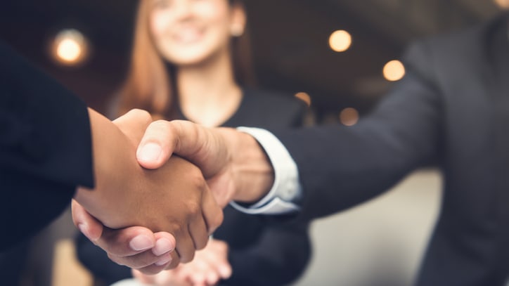 Two business people shaking hands in front of a group of people.