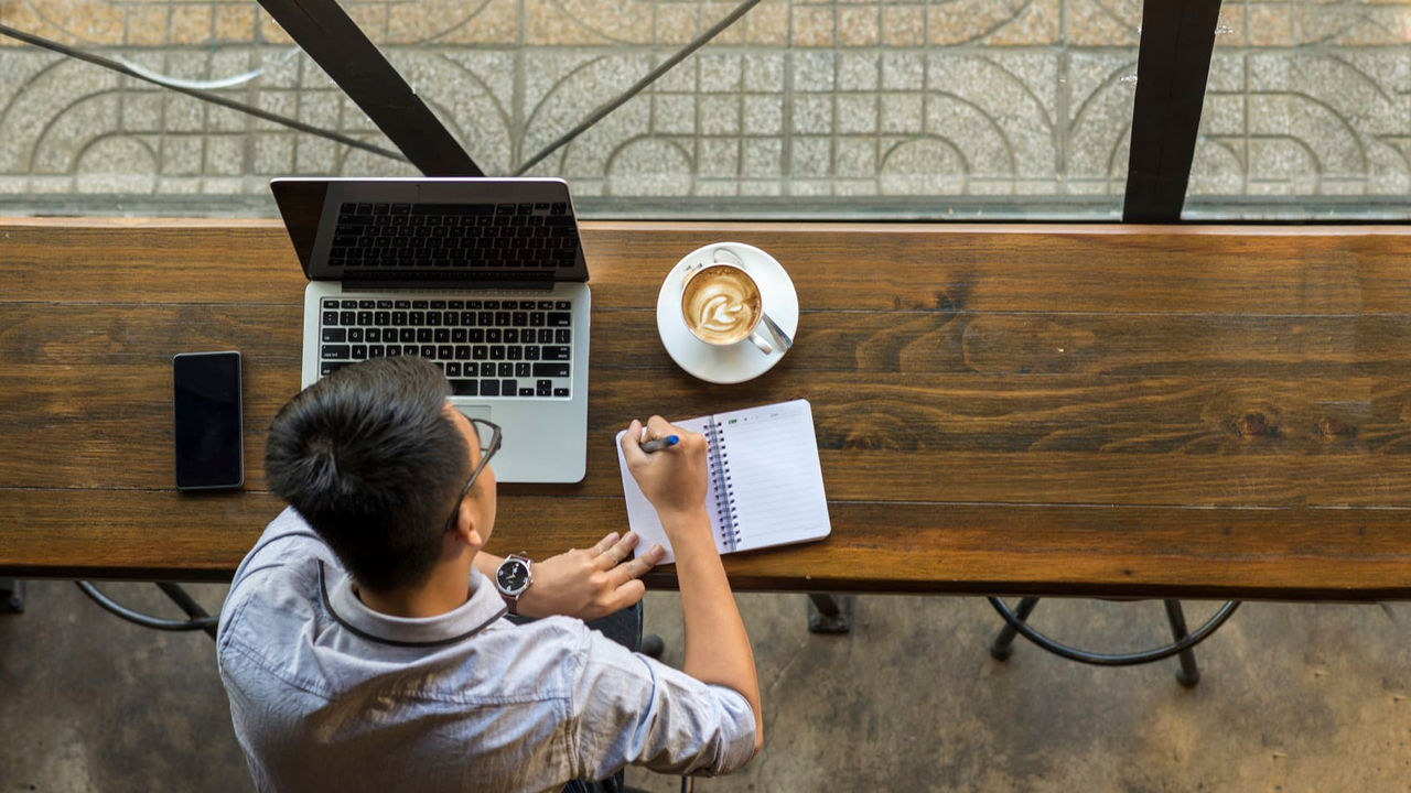 A man sitting at a table with a laptop and coffee.