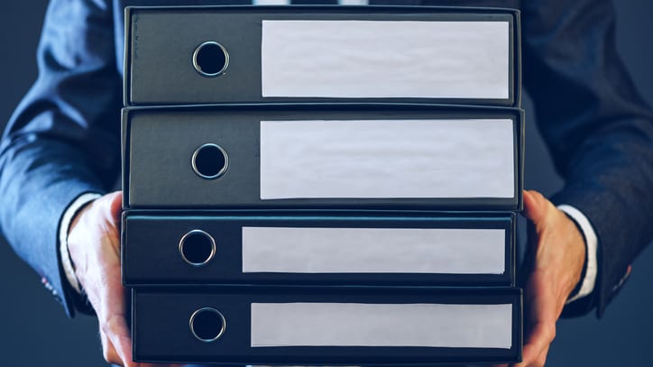 A businessman is holding a stack of binders.