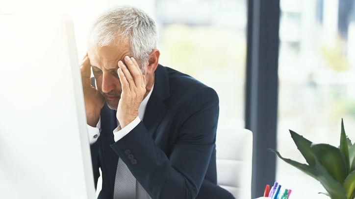 A man in a suit is holding his head in front of a computer.