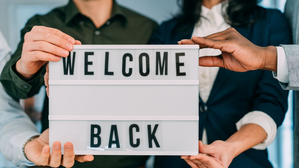 A group of business people holding up a welcome back sign.