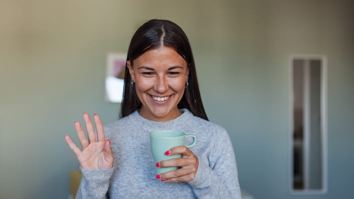 A woman holding a cup of coffee in front of a laptop.