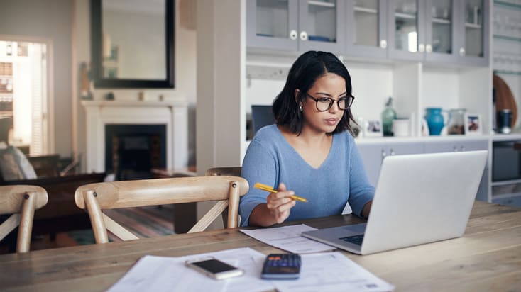 A woman sitting at a table with a laptop and papers.