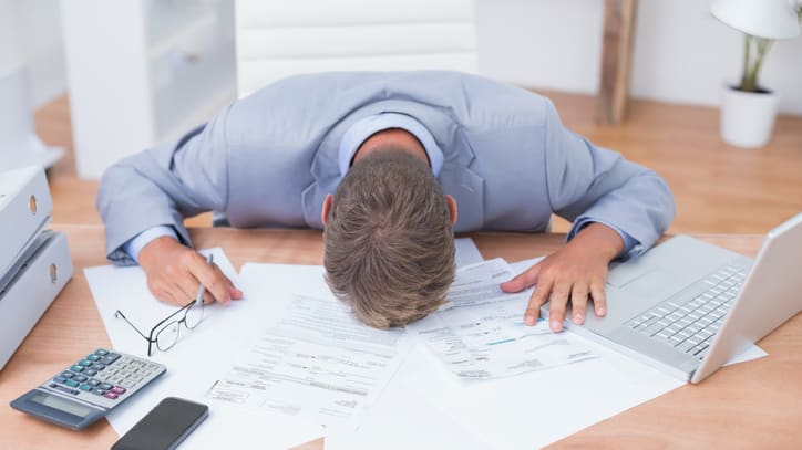 A man in a suit is sitting at his desk with papers and a laptop.