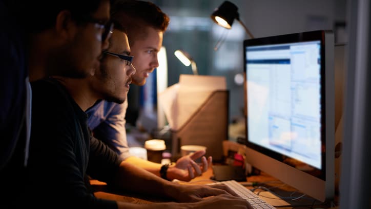 Three men looking at a computer screen.