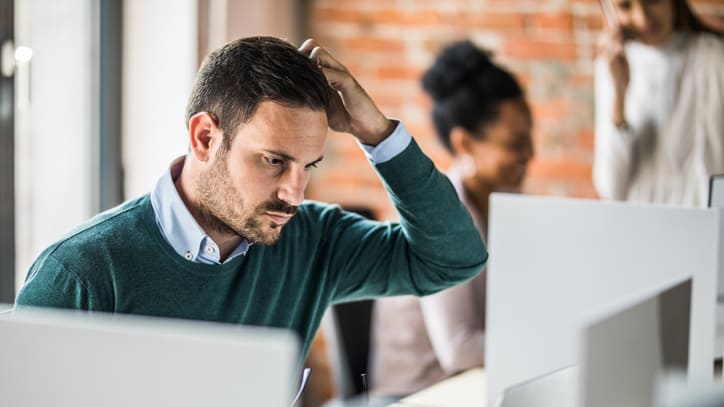 A man is holding his head in front of a group of computers.