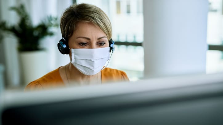 A woman wearing a surgical mask while working on a computer.