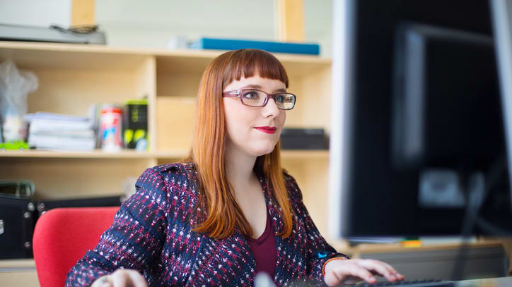 A woman in glasses is working on a computer.