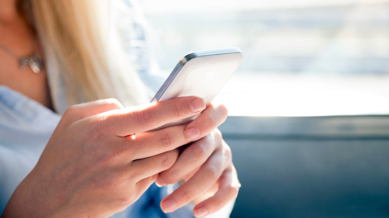 A woman is holding a cell phone while sitting on a train.