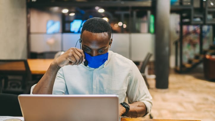 A man wearing a face mask while working on a laptop.