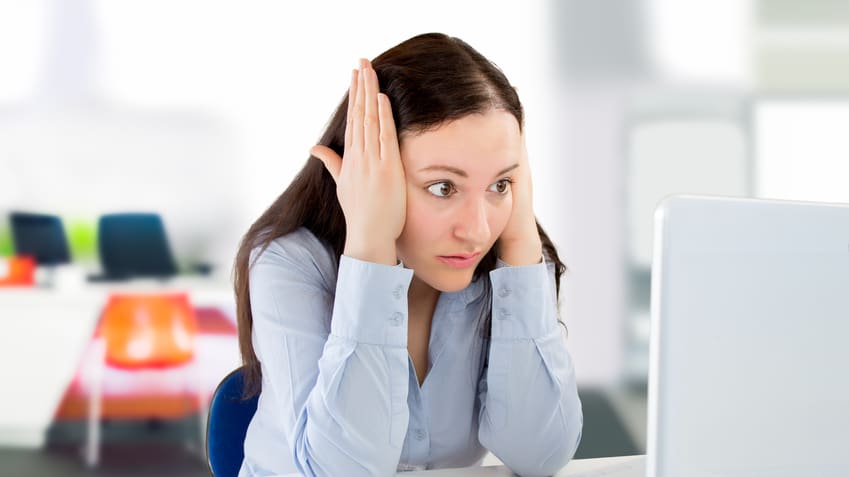 A woman with her hands on her head in front of a laptop.