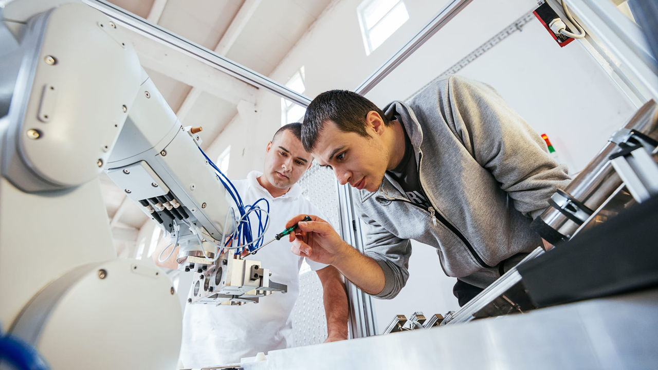 Two men working with a robot in a factory.