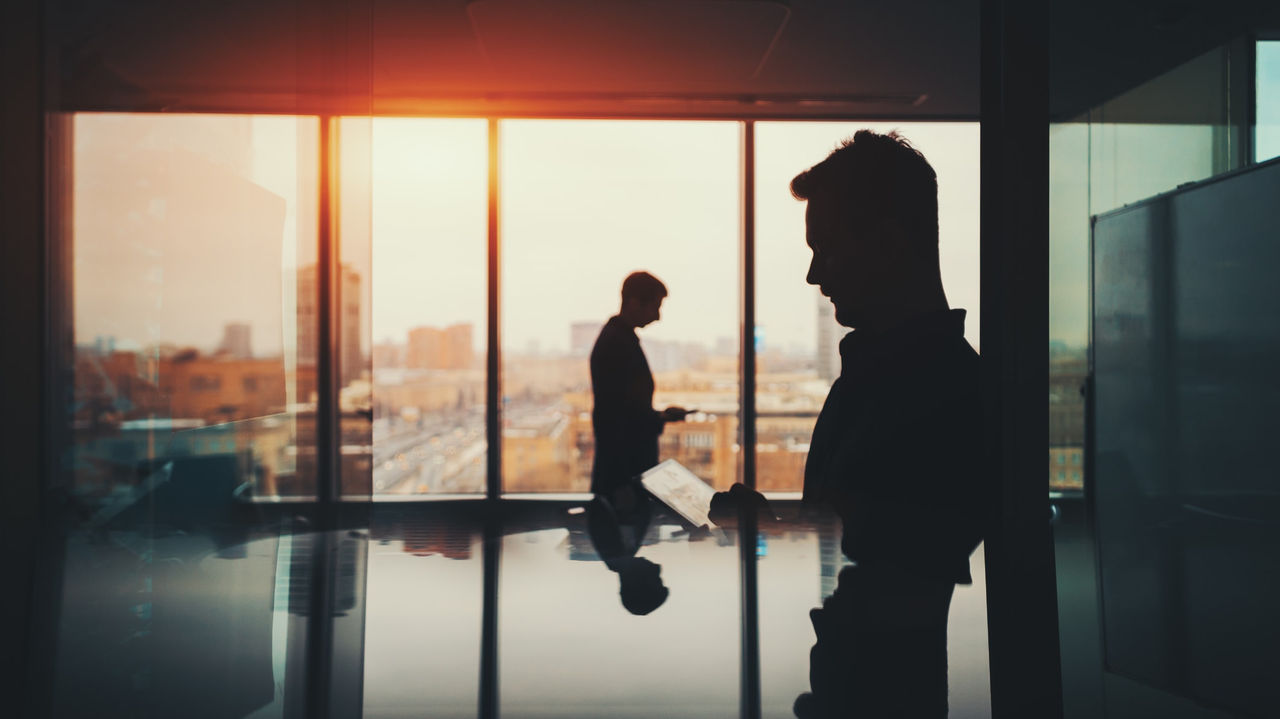 Silhouette of two businessmen standing in front of a window.