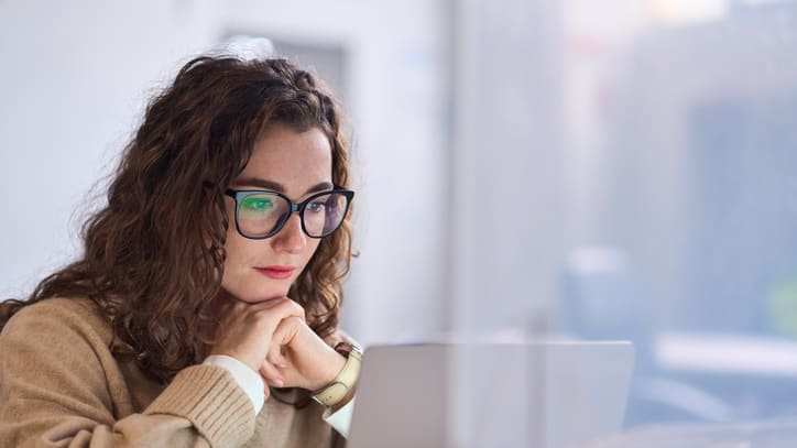 A woman wearing glasses is looking at her laptop.