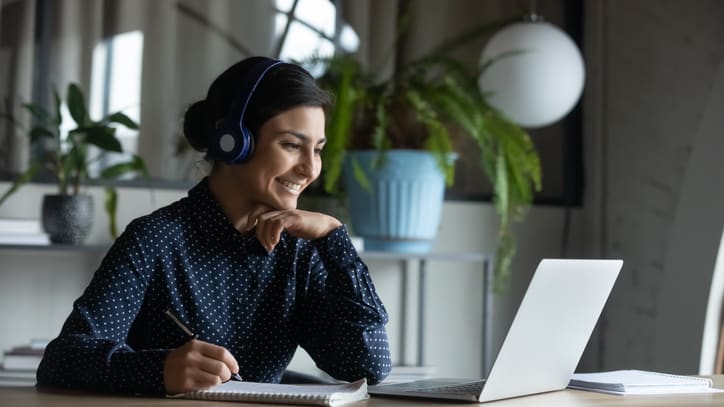 A woman wearing headphones is sitting at a desk with a laptop.