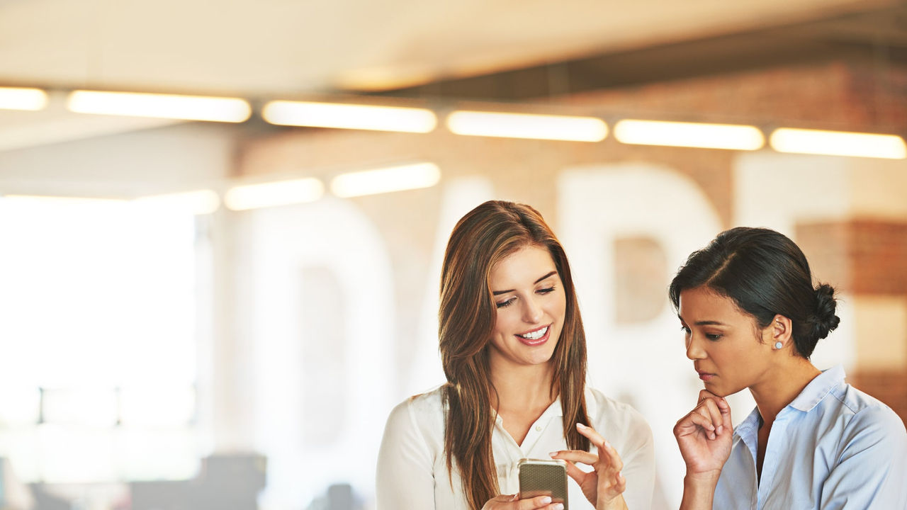 Two women looking at a cell phone in an office.