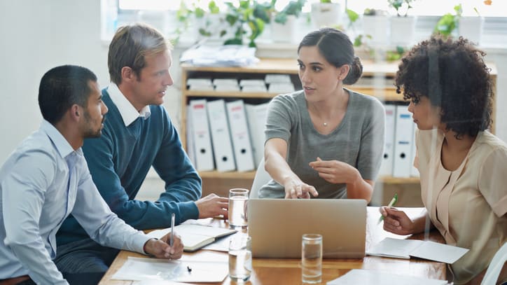 A group of people sitting around a table with a laptop.