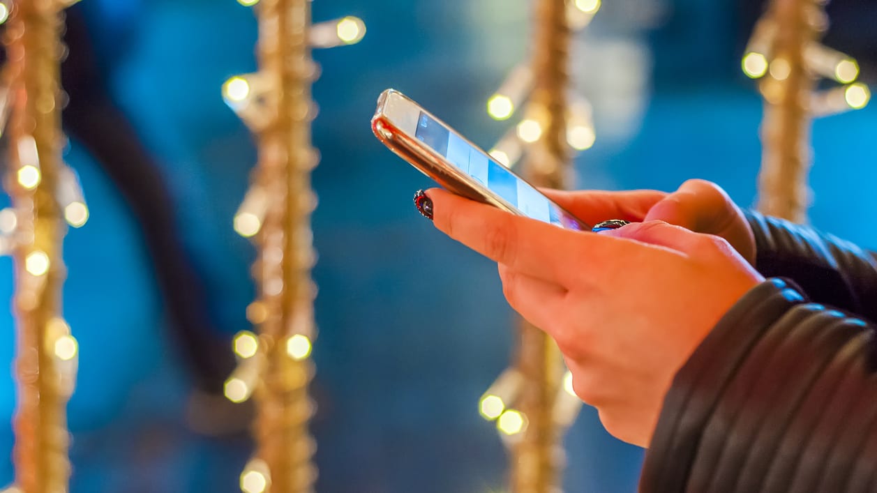 A woman is using a cell phone in front of christmas lights.
