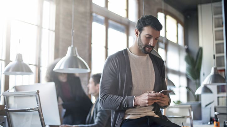 A man sitting in an office looking at his phone.