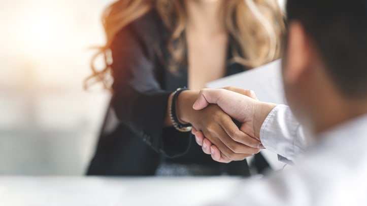 A businessman and woman shaking hands in front of an office.