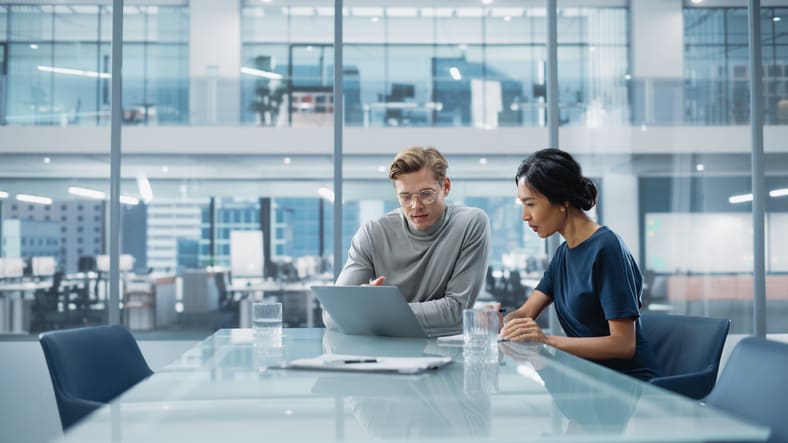 Two business people sitting at a table looking at a laptop.