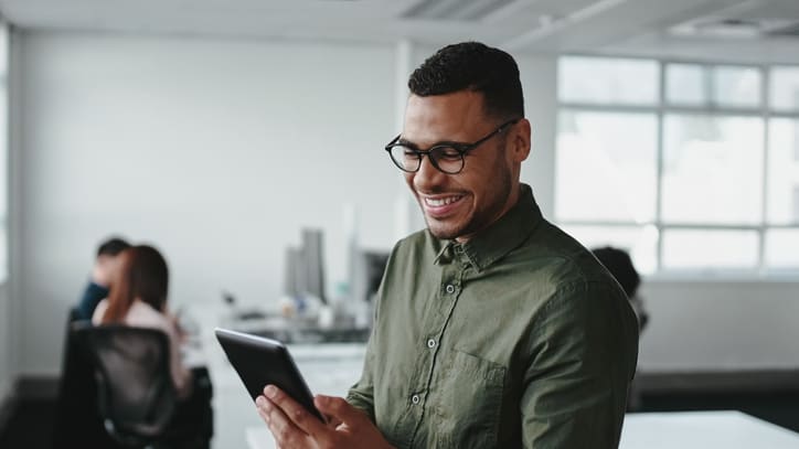 A man in glasses is using a tablet in an office.