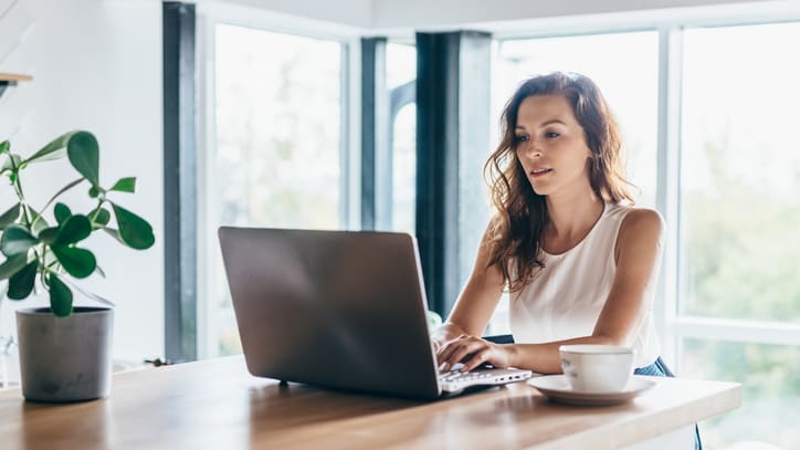 A woman working on her laptop in front of a potted plant.