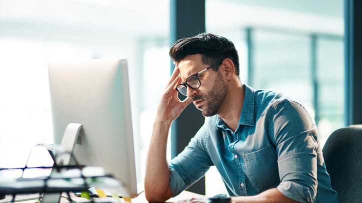 A man sitting in front of a computer with his head in his hands.