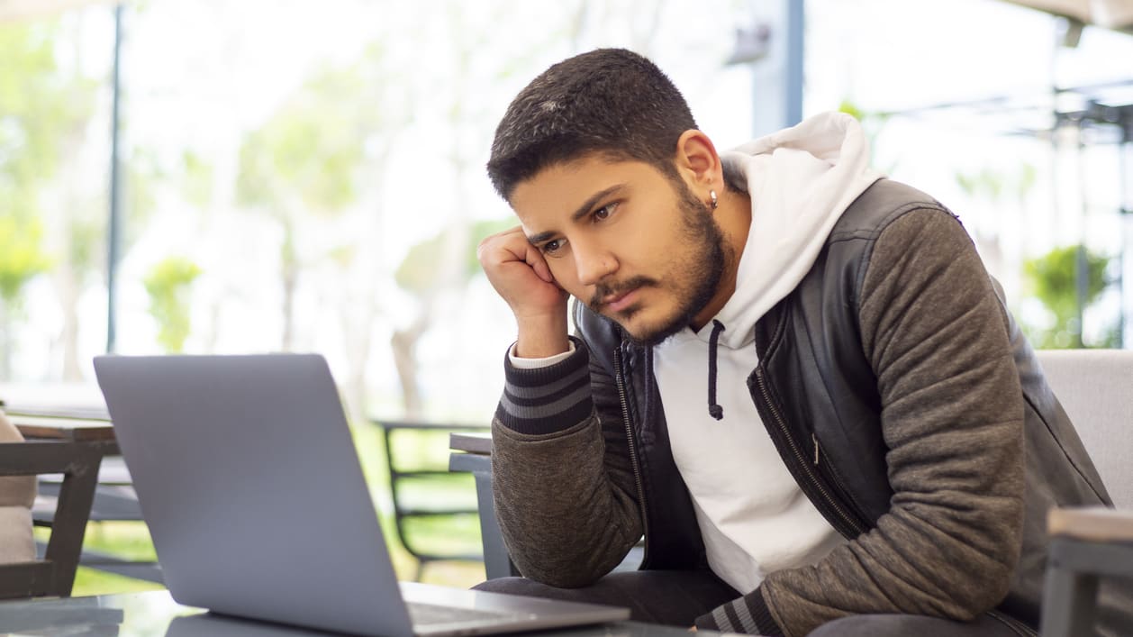 A man sitting at a table looking at his laptop.