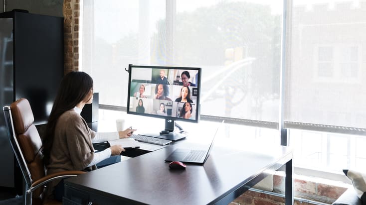 A woman sits at a desk and uses a video conferencing system.