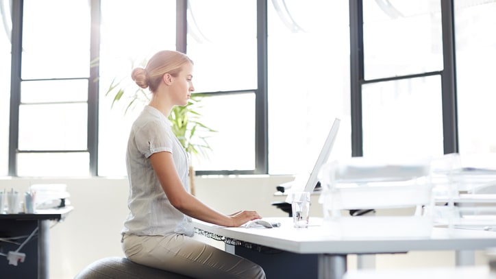 A woman sitting on an exercise ball in an office.