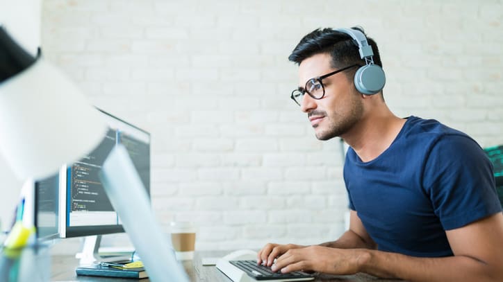 A man wearing headphones is working on a laptop.